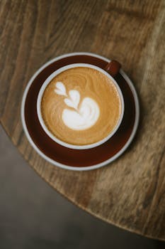 Top view of a beautifully crafted latte with art in a ceramic cup on a wooden table, creating a warm ambiance.