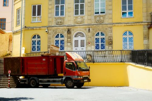 Free A red truck parked in front of a historic yellow building facade in an urban setting. Stock Photo
