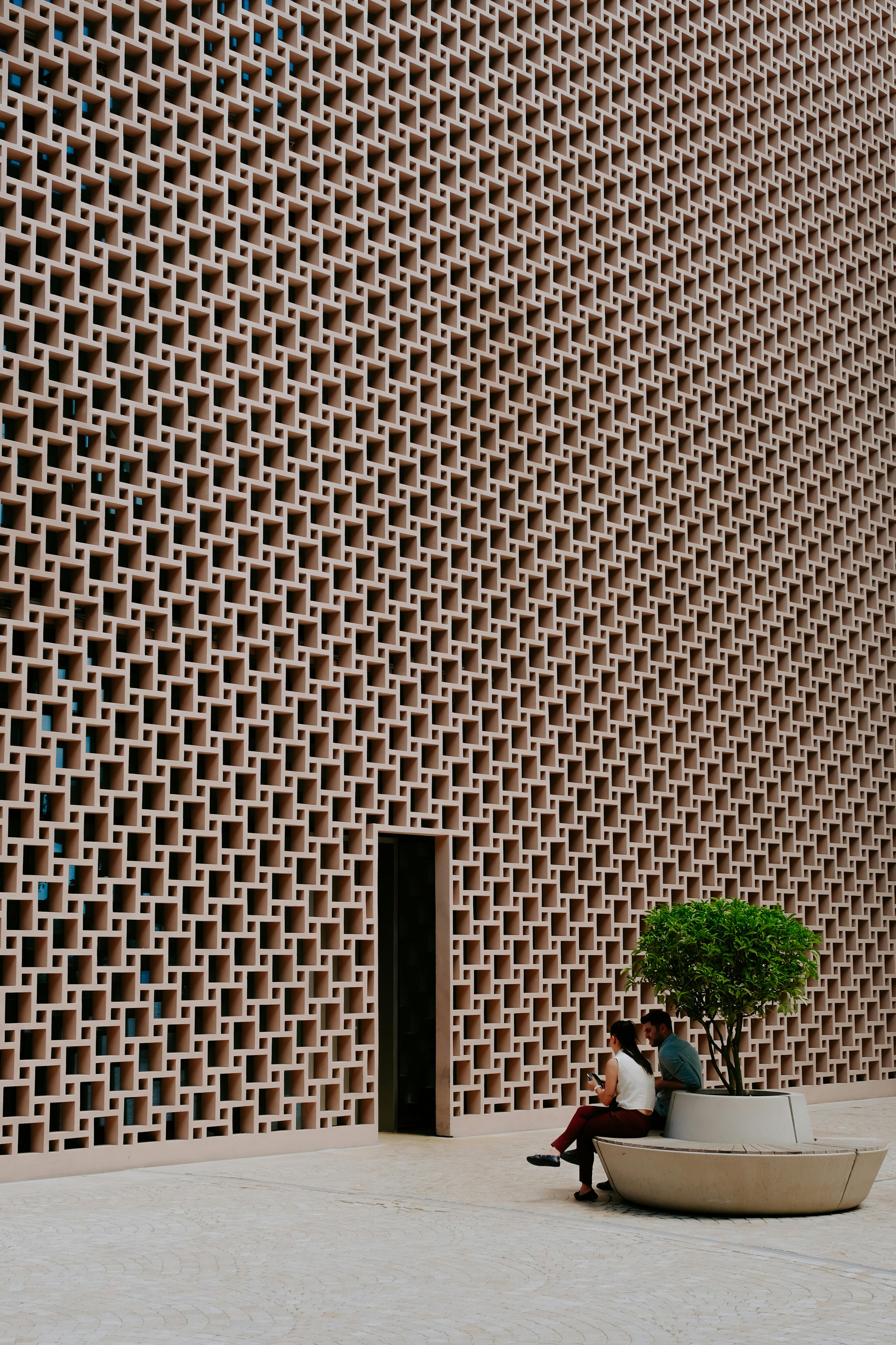 Two people sitting on a bench by a geometric wall, offering urban minimalism vibes.