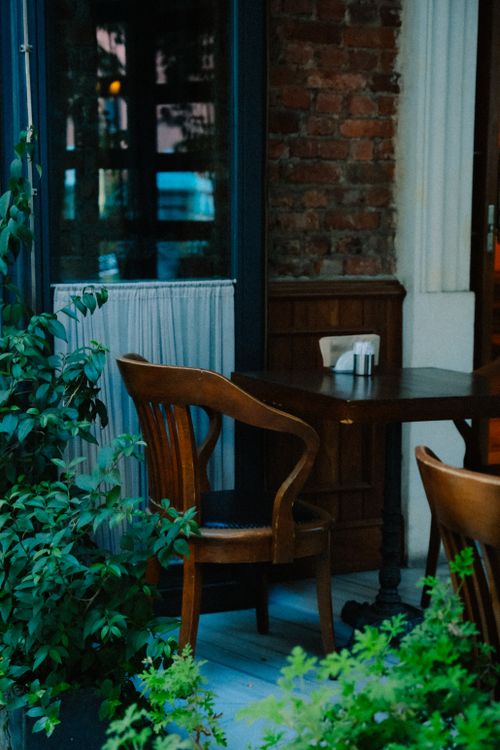 Free A charming outdoor cafe setting featuring wooden chairs, a table, and lush greenery. Stock Photo
