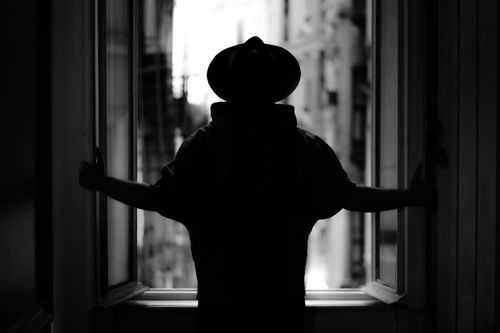 Free Black and white silhouette of a person in a hat at a window gazing at the cityscape. Stock Photo