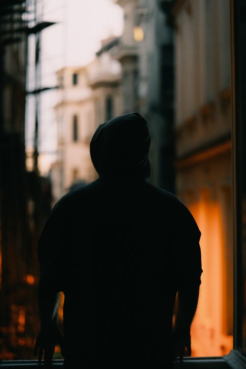 Free Silhouette of a person in an urban street setting with warm sunset light creating a dramatic mood. Stock Photo