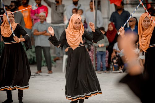 Women in Orange Headscarves Performing Traditional Dance Tapping the Rhythm with Sticks at a Festival