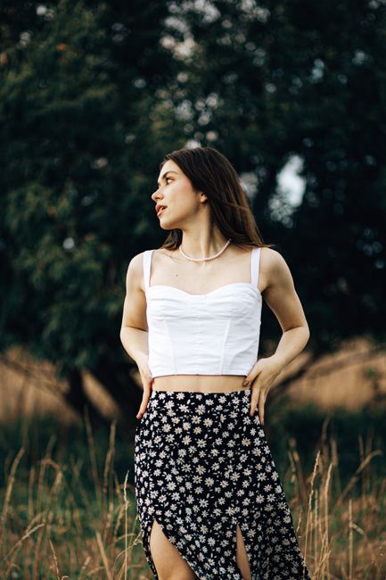 Stylish woman wearing a white blouse and floral skirt in a natural setting.