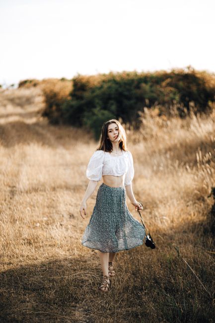 A fashionable woman walking in a serene countryside setting during summer.