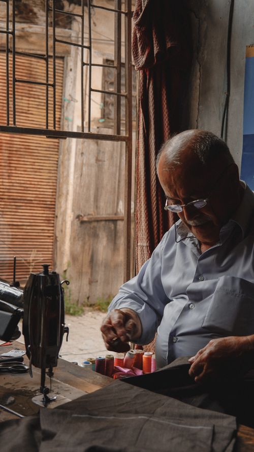Free An elderly man focused on sewing in a rustic indoor workshop. Ideal for lifestyle and craft themes. Stock Photo