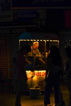 A street vendor in İzmir serves hot dogs at night under warm streetlight glow.