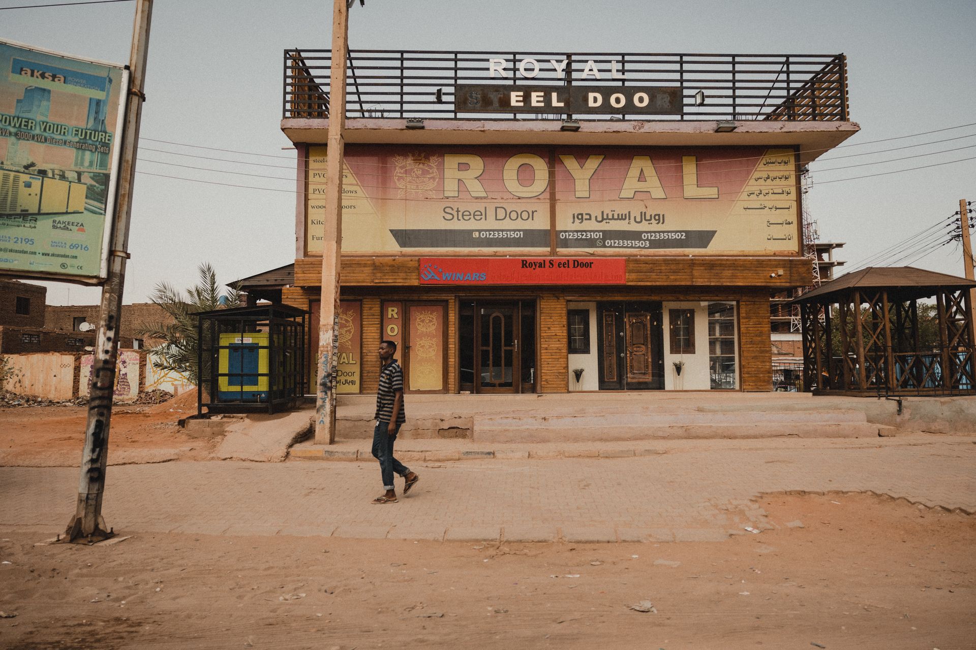 A man walks past an empty storefront with a prominent 'Royal Steel Door' sign on a quiet street.