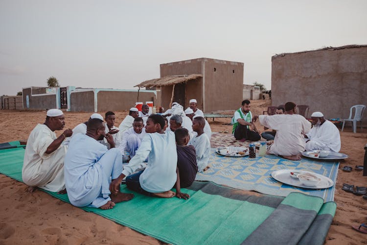 Photo Of Eating Men Sitting On Blankets