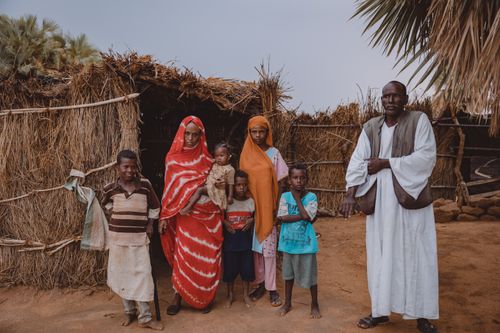 Free A family stands together outside a traditional thatch-roofed hut in an African village. Stock Photo