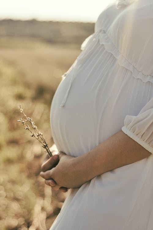 Pregnant Woman in White Dress with Hands on Belly