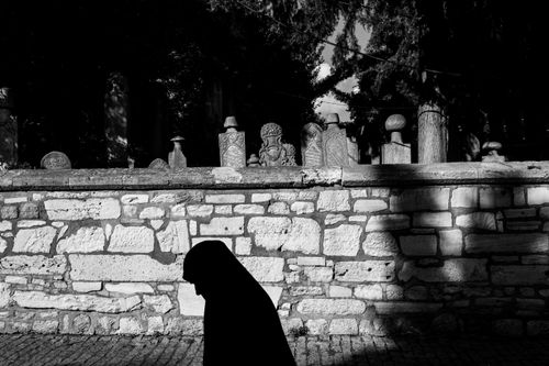 Free A woman in silhouette walks by ancient tombstones in Istanbul, captured in black and white. Stock Photo