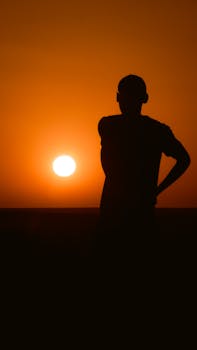 A striking silhouette of a man during a dramatic sunset in Adrar, Algeria, showcasing a golden glow.