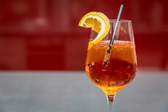 Orange spritz cocktail with ice in a wine glass with an orange slice and straw