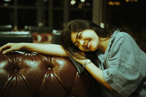 Free Happy woman leaning on a leather couch with a warm smile, creating a cozy indoor atmosphere. Stock Photo