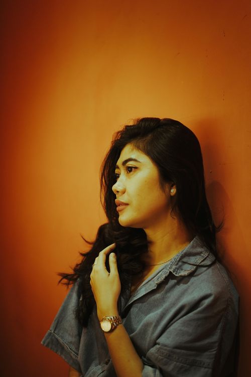 Free Profile portrait of a woman in a denim shirt against an orange wall, conveying a calm mood. Stock Photo