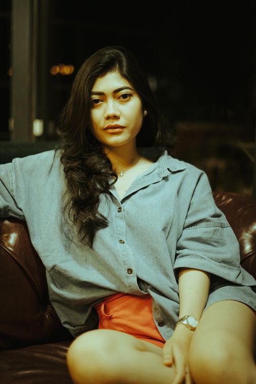 Free Young woman in casual attire sitting on a leather couch indoors. Stock Photo