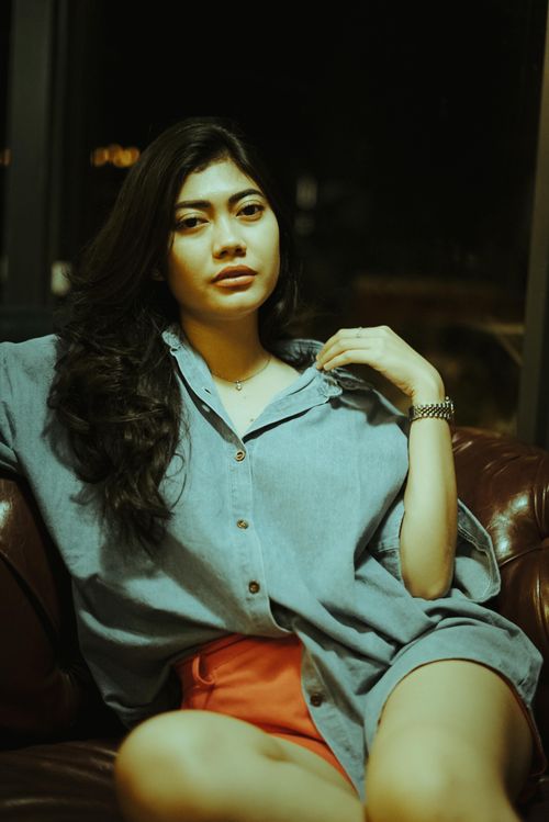 Free Asian woman in a relaxed pose on a leather couch, stylish and serene indoor setting. Stock Photo