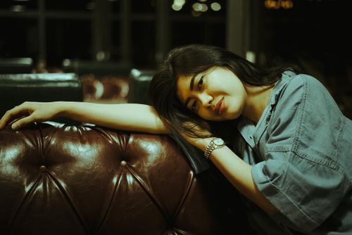 Free A serene woman in casual attire rests on a luxurious leather sofa in a dimly lit room. Stock Photo
