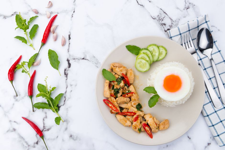 Delicious Thai basil chicken with rice and fried egg, styled on marble.