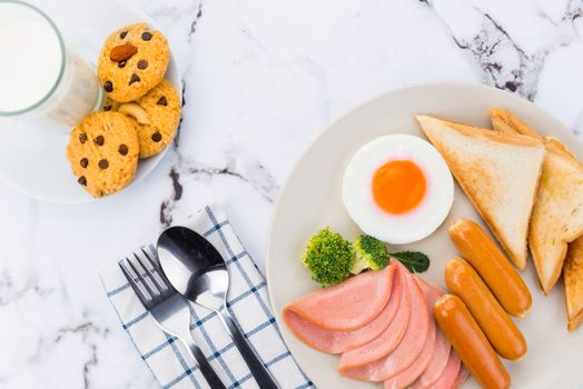 A close-up of a breakfast platter with egg, sausages, ham, toast, cookies, and milk.