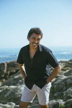 A joyful man stands by the ocean, smiling and enjoying a sunny day at the beach.