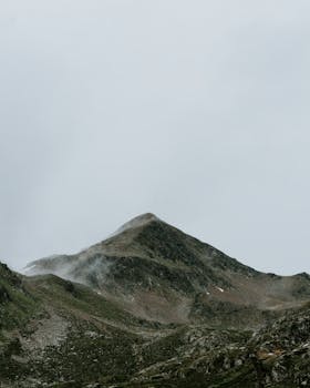 Serene mountain peaks shrouded in fog and mist under a cloudy sky.