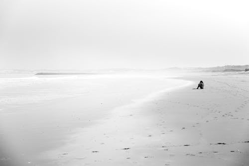 Grayscale Photo of a Person Sitting on Shore