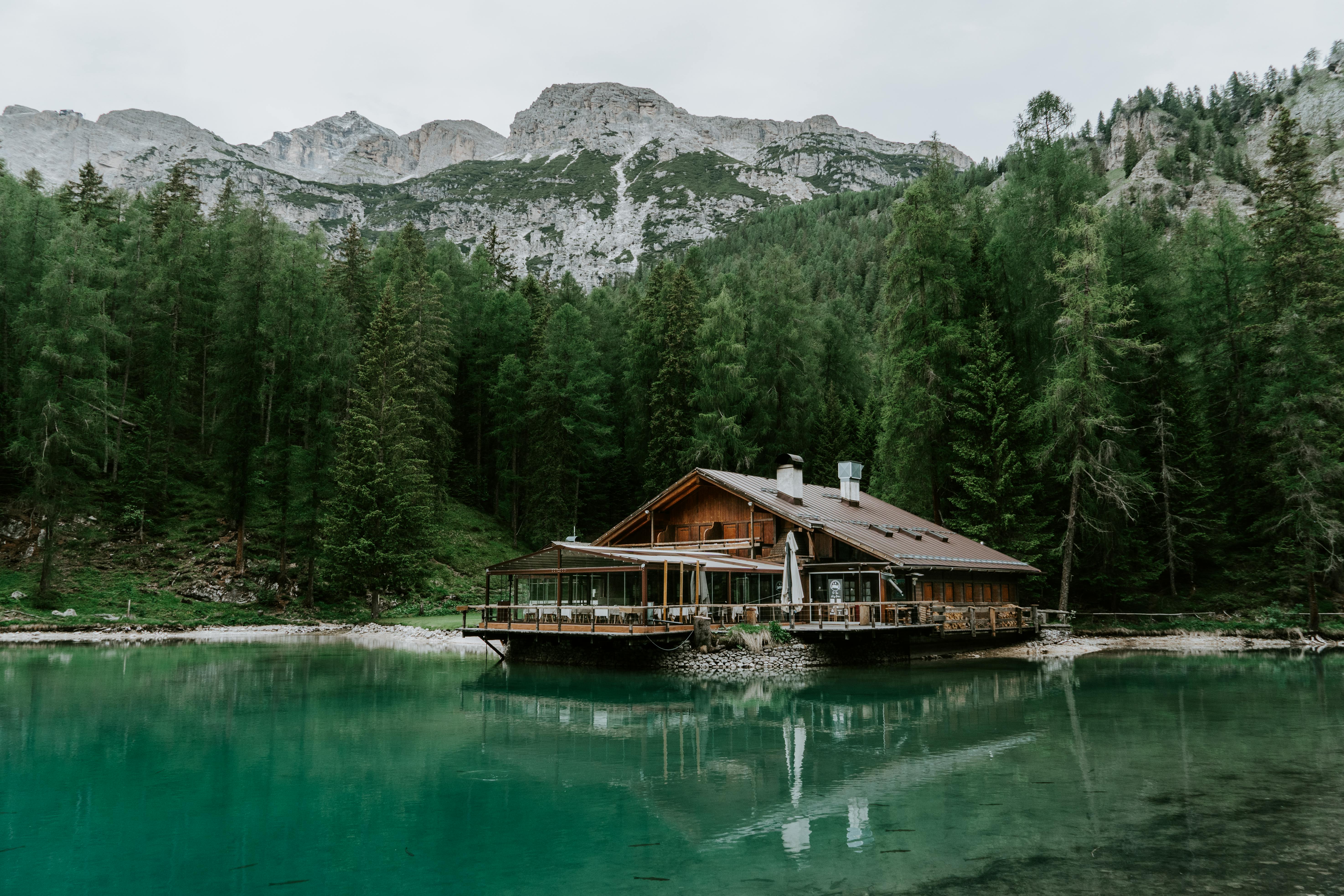 Idyllic cabin by a peaceful lake with mountain backdrop and lush forest.
