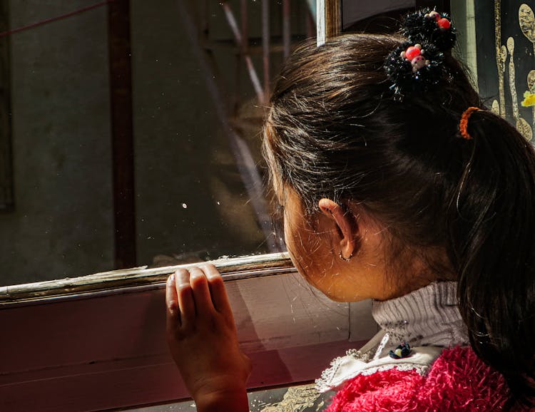 Girl In Ponytail Looking Outside A Glass Window