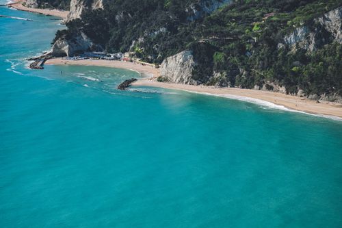 Free Breathtaking aerial shot of a serene turquoise beach bordered by cliffs and lush greenery. Stock Photo