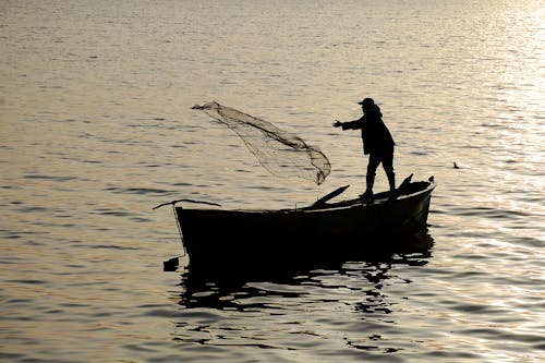 Man Standing on Boat Throwing Fishing Net to the Sea