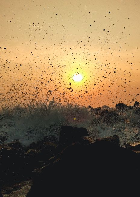 Fotomural Toma cautivadora de olas del océano rompiendo contra rocas al atardecer, creando un impresionante salpicón de agua.