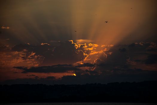 A stunning sunset with radiant sky rays highlighting dramatic clouds over a silhouetted landscape.