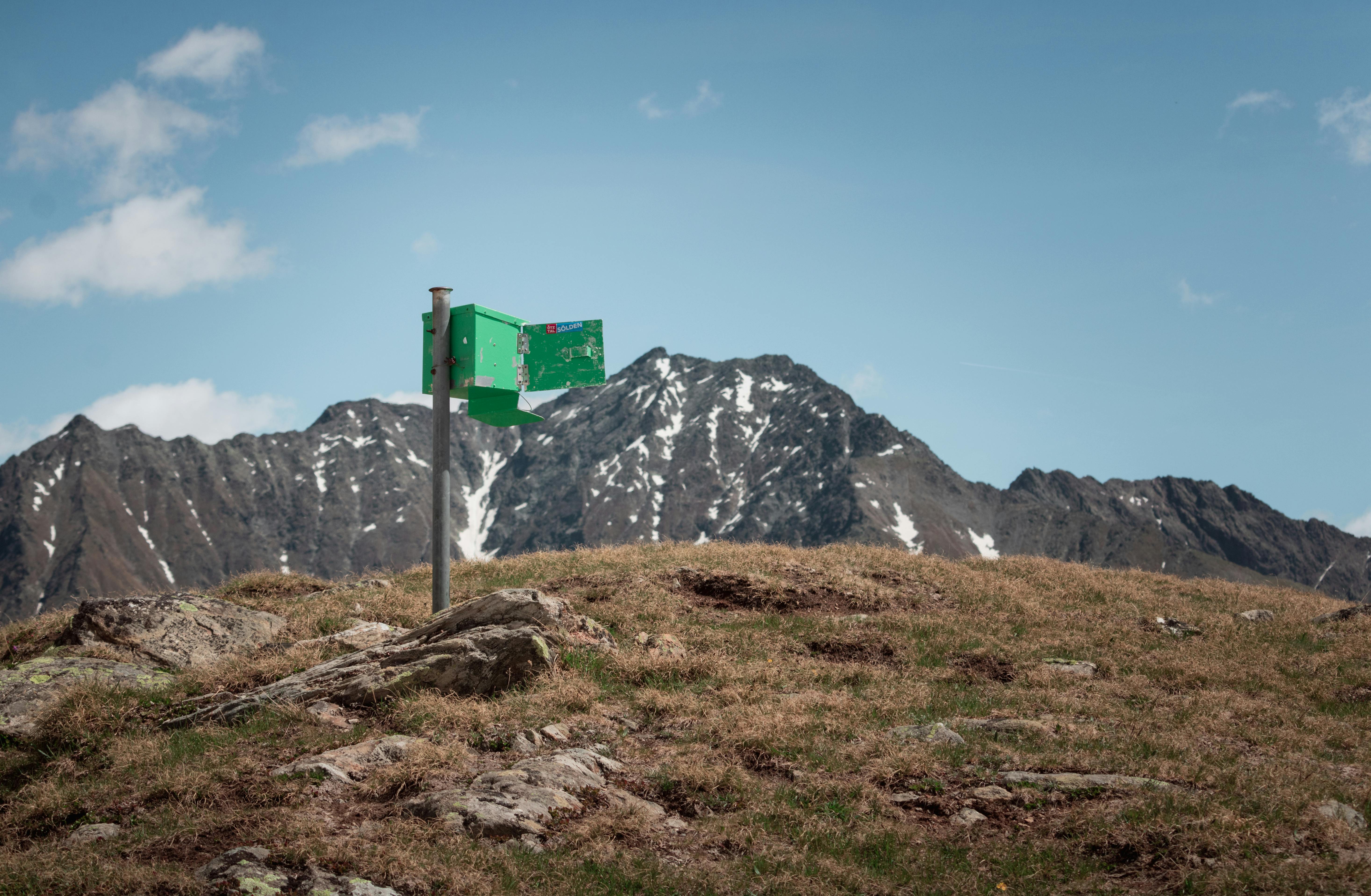 green and white signage on green grass field near gray rocky mountain under blue sky during