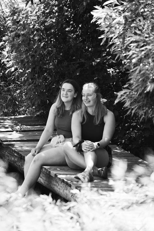 Two Women Sitting on the Wooden Dock in Grayscale Photography