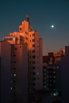 City skyline at night with tall buildings and a glowing moon in the background.