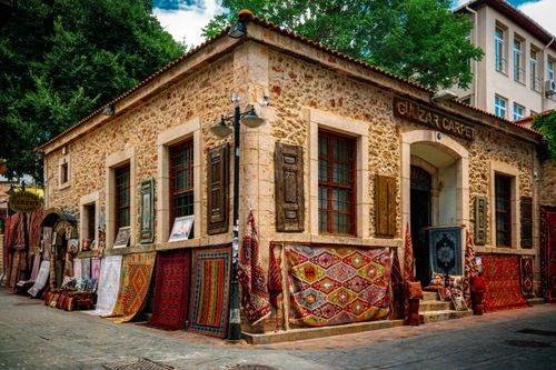 Free A rustic stone building displaying vibrant carpets and textiles on a sunny street. Stock Photo