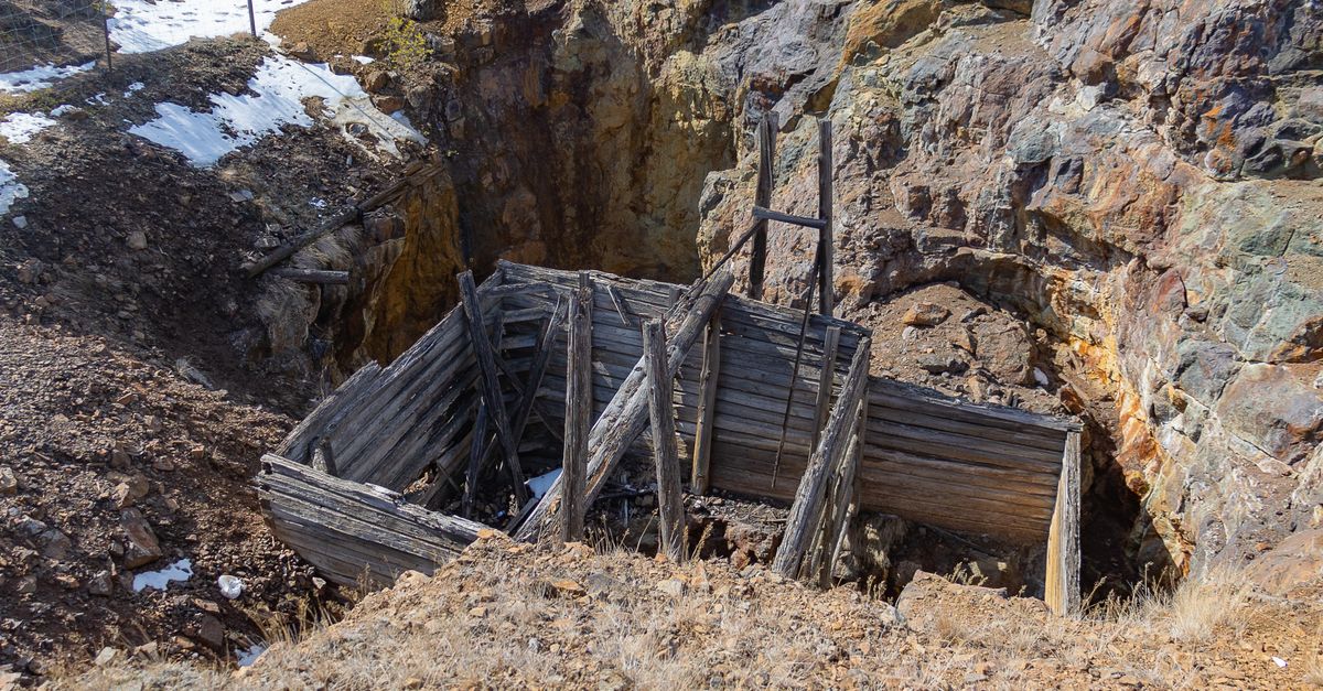 An abandoned wooden mine entrance set in a rural rocky landscape with patches of snow.
