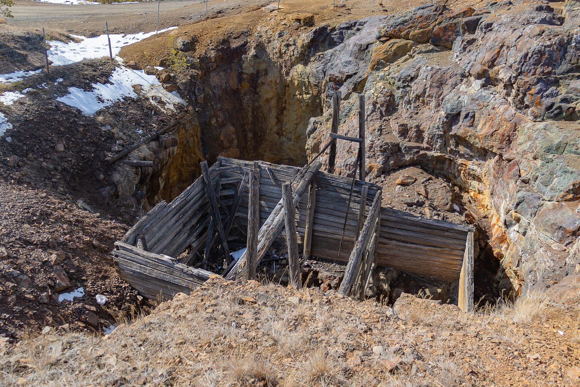 An abandoned wooden mine entrance set in a rural rocky landscape with patches of snow.