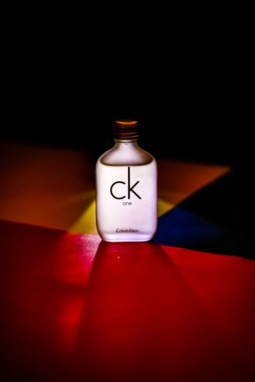 Free Product shot of CK One perfume, showcased on a multi-colored surface with dramatic lighting. Stock Photo