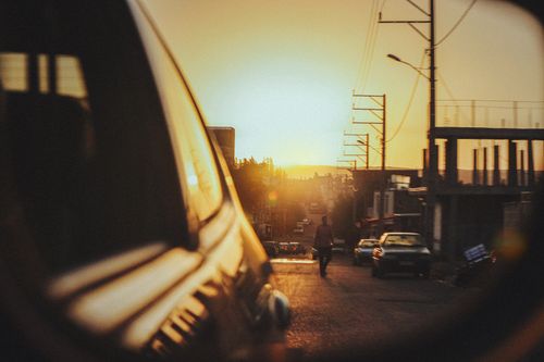 Free A city street captured at sunset with reflections on a car's rearview mirror. Stock Photo