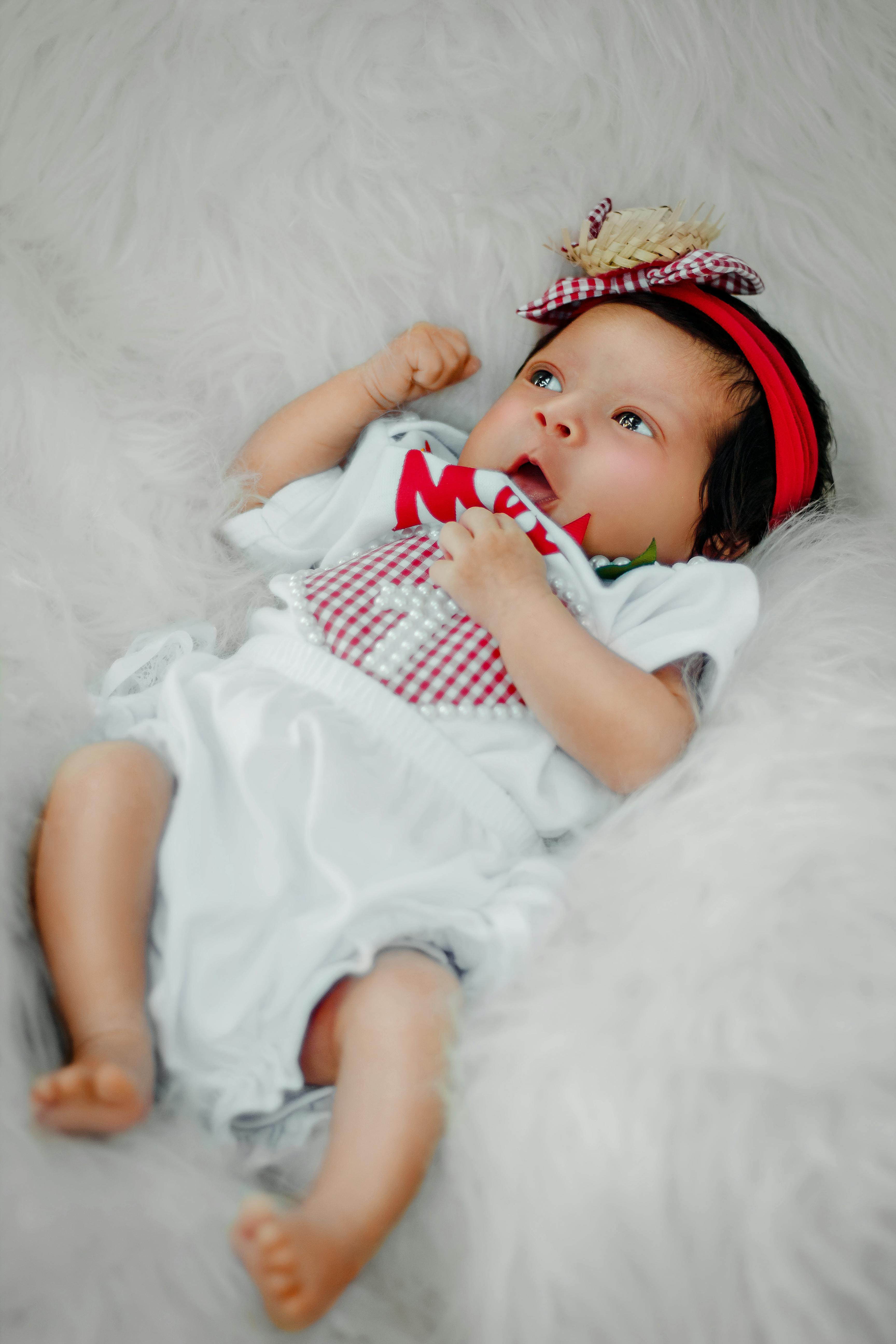 baby girl in white dress lying on white textile