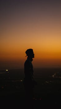 Dramatic silhouette of a man wearing a cap against a vibrant sunset over Panama City skyline.