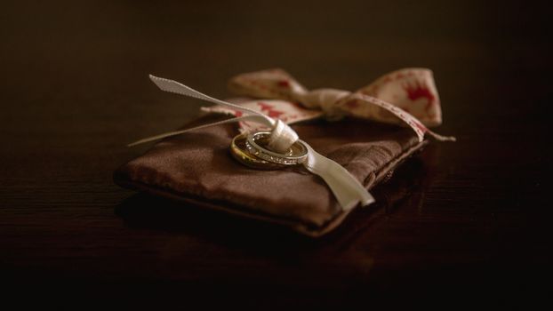 Close-up of wedding bands on a brown satin pouch with ribbons on a wooden surface.
