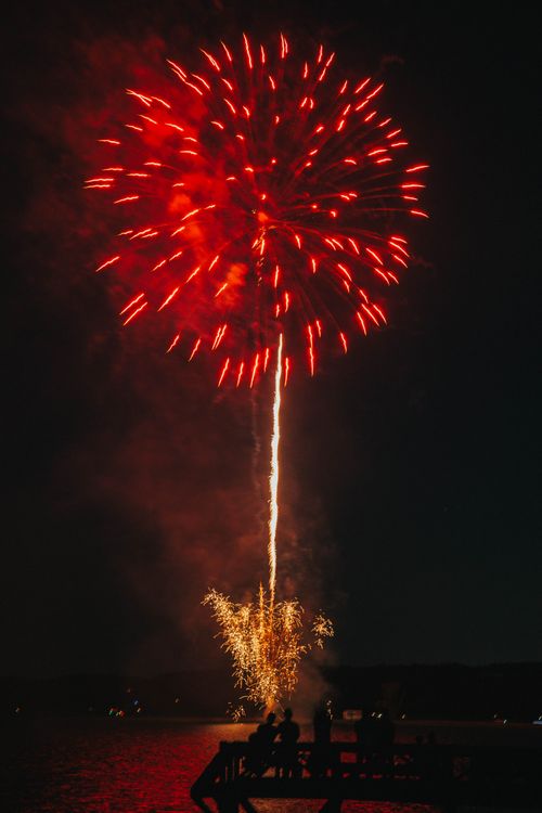 Free Vibrant red fireworks illuminating the night sky over a lake, creating a dazzling display in Conway, AR. Stock Photo