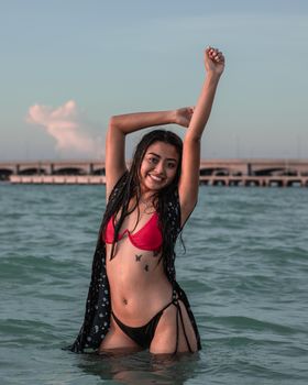 Asian woman with tattoos posing playfully in the ocean during a sunny day.