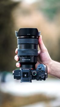 A detailed view of a DSLR camera held in hand with a blurred outdoor background.