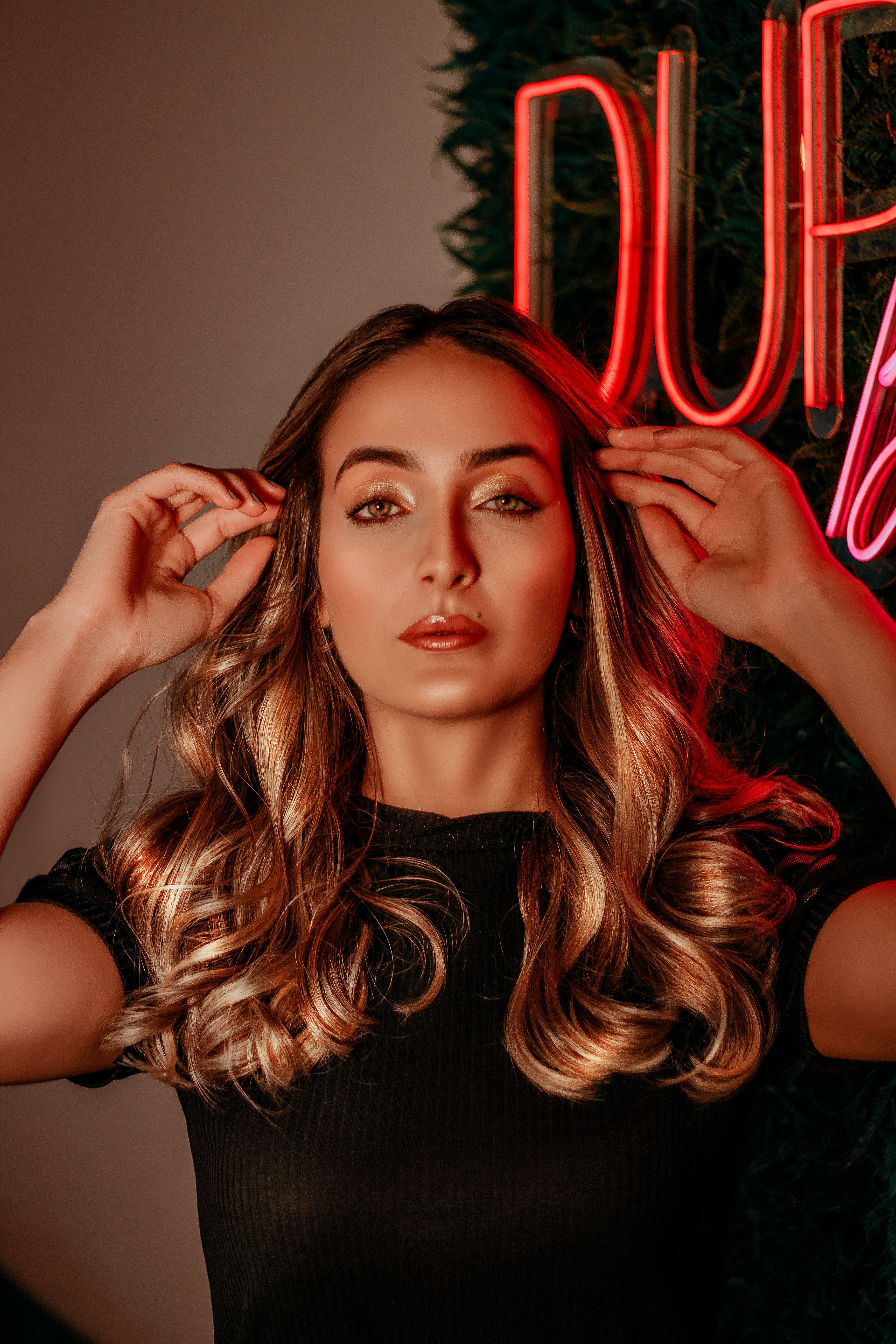 Fotomural Mujer de moda con cabello rubio ondulado posa con confianza frente a una señalización de neón, irradiando elegancia moderna.
