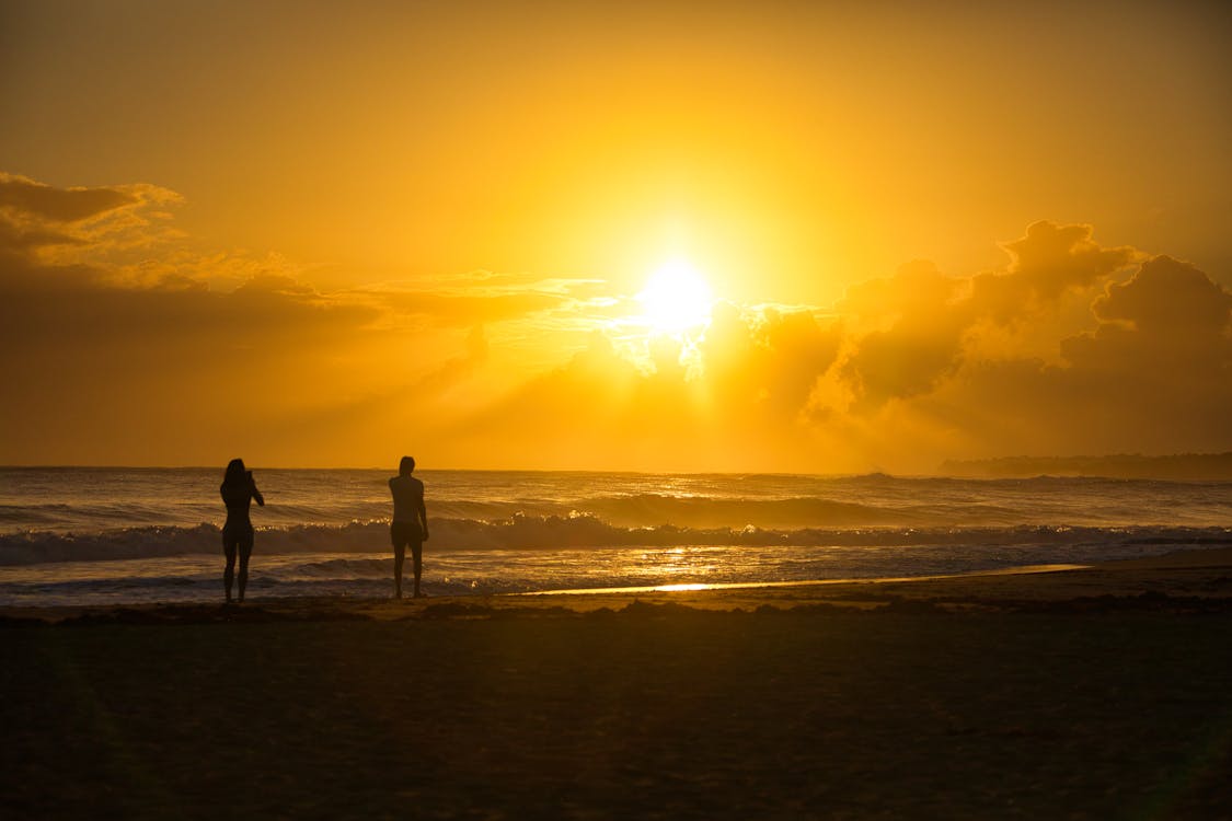 Silhouette of Two People Standing on Beach under a Golden Sky